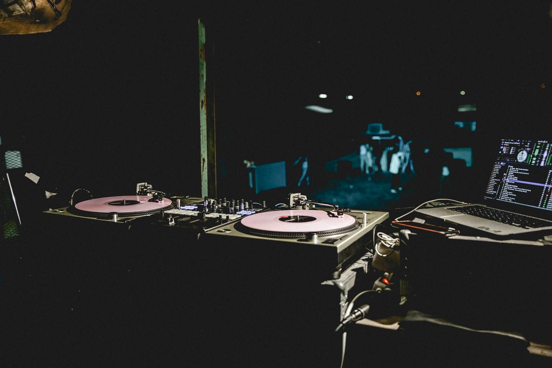 DJ at a booth with headphones and laptop reviewing music tracks